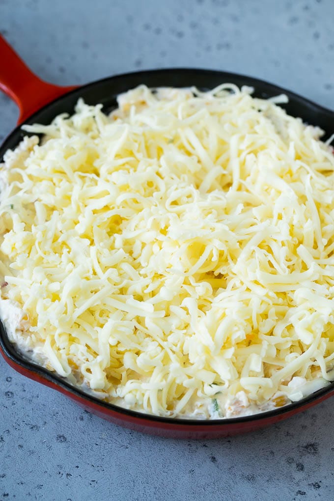 Corn Dip Recipe | Hot Cheese Dip | Bacon Dip #corn #dip #bacon #cheese #appetizer #snack #sadud A skillet of corn dip covered with shredded cheese.
