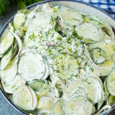 Creamy cucumber salad with red onion and dill, topped with fresh herbs for garnish.