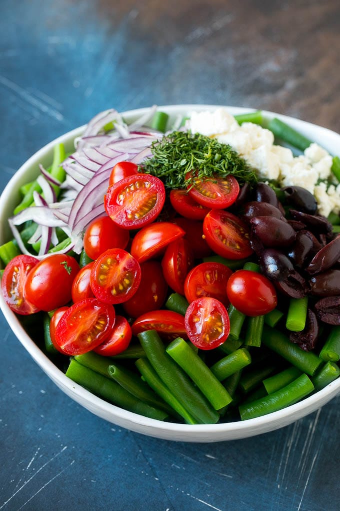 Green Bean Salad Recipe | String Bean Salad | Chopped Salad #greenbeans #tomatoes #olives #salad #cleaneating #lowcarb #glutenfree #sadud Vegetables like cherry tomatoes, red onion and olives in a bowl with feta cheese.