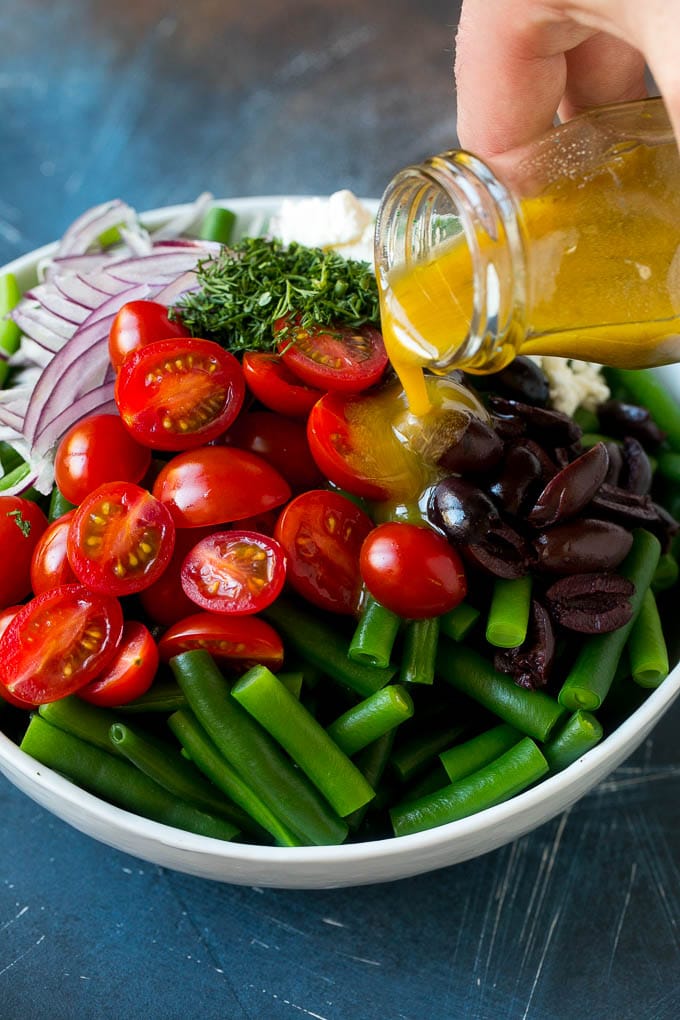 Green Bean Salad Recipe | String Bean Salad | Chopped Salad #greenbeans #tomatoes #olives #salad #cleaneating #lowcarb #glutenfree #sadud Dressing being poured over veggies like cherry tomatoes, olives and onions.