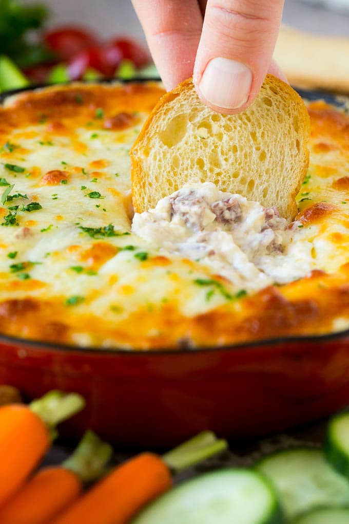 Reuben Dip Recipe | Corned Beef Dip | Cheese Dip #dip #cheese #cornedbeef #appetizer #lowcarb #keto #sadud A baguette chip dipping into a skillet of Reuben dip.