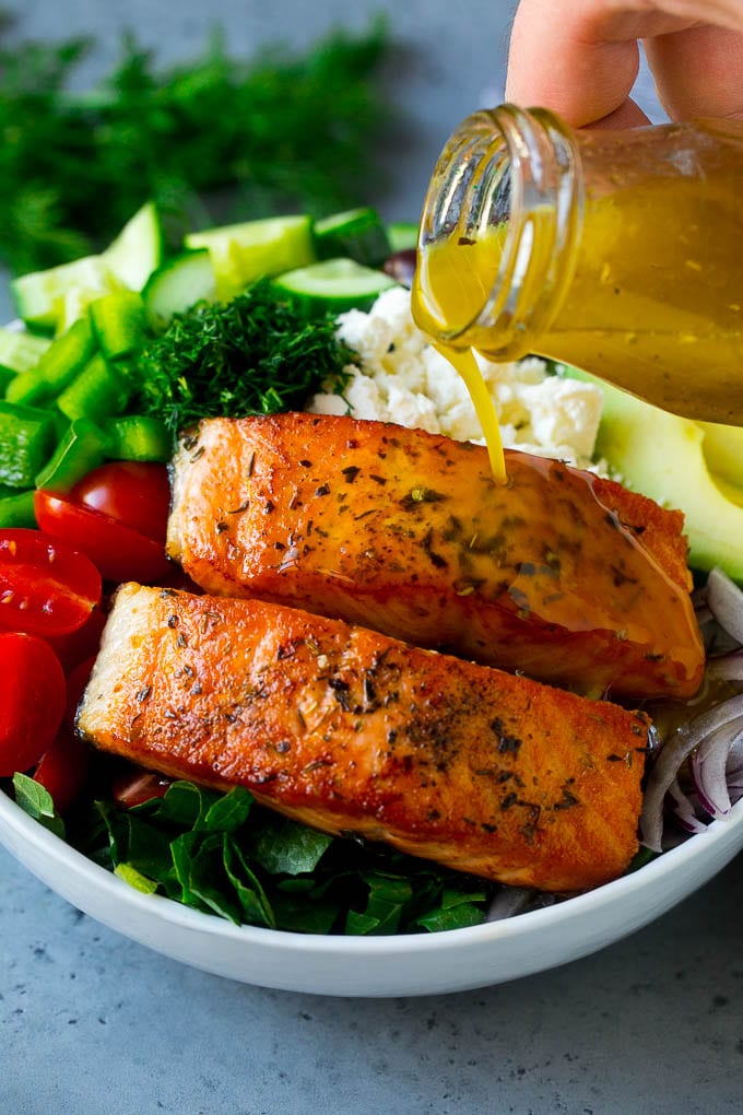 Greek Salmon Salad Recipe | Low Carb Salmon Recipe | Salmon Salad #salmon #seafood #fish #lowcarb #keto #lunch #sadud #healthy Salmon fillets on top of greens with dressing being poured over the top.