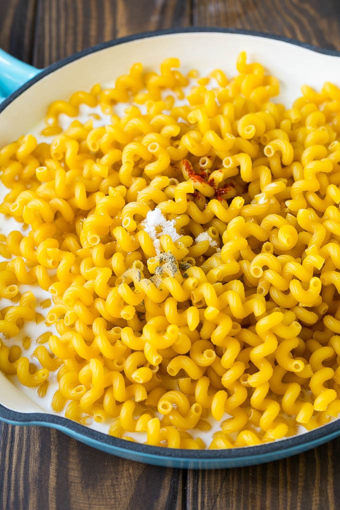 This baked mac and cheese is a blend of tender noodles in a rich and creamy cheese sauce. Uncooked pasta and spices with milk in a pan.