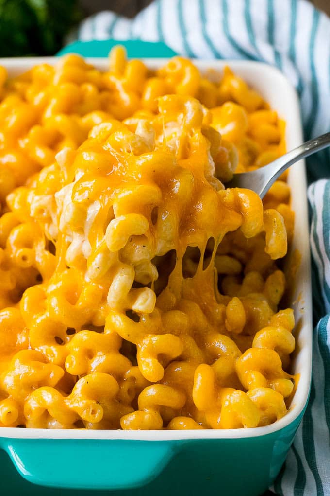 This baked mac and cheese is a blend of tender noodles in a rich and creamy cheese sauce. Baked mac and cheese with a serving spoon lifting up a portion.