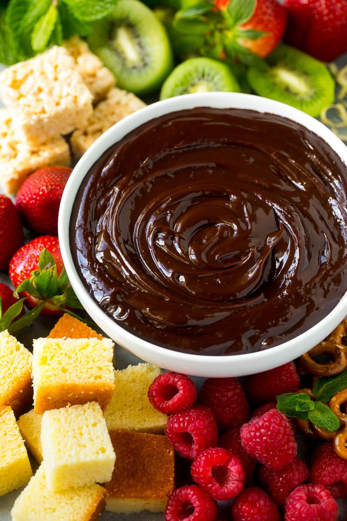 Chocolate Fondue Recipe | Chocolate Sauce | Chocolate Dip #chocolate #dessert #glutenfree #fondue #sadud A bowl of chocolate fondue surrounded by fruit, cake, rice krispy treats and pretzels.