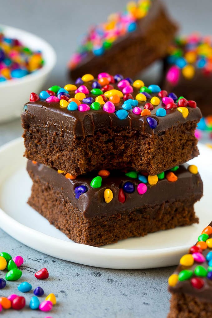 Cosmic Brownies Recipe | Cocoa Brownies | Frosted Brownies #brownies #chocolate #dessert #sadud #sprinkles A stack of cosmic brownies on a plate with a bite taken out of one.