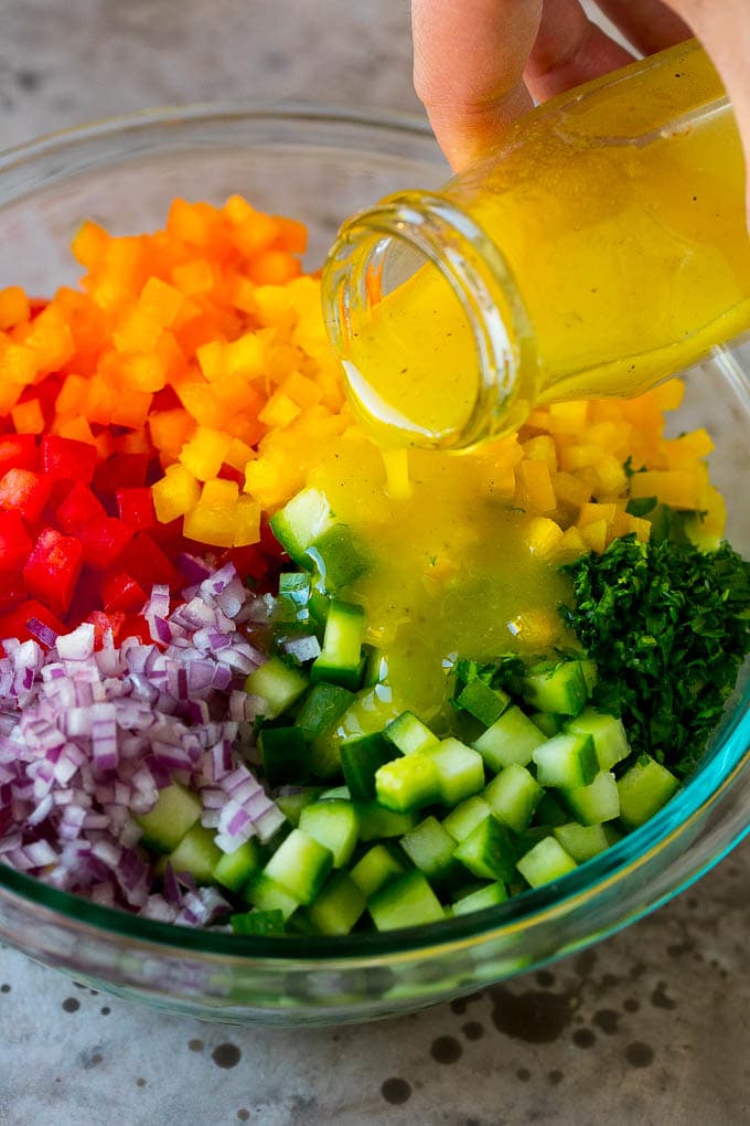 Israeli Salad Recipe | Cucumber Salad | Tomato Salad | Chopped Salad #salad #cleaneating #healthy #glutenfree #lowcarb #keto #sidedish #lunch #sadud Lemon dressing being poured over chopped vegetables.