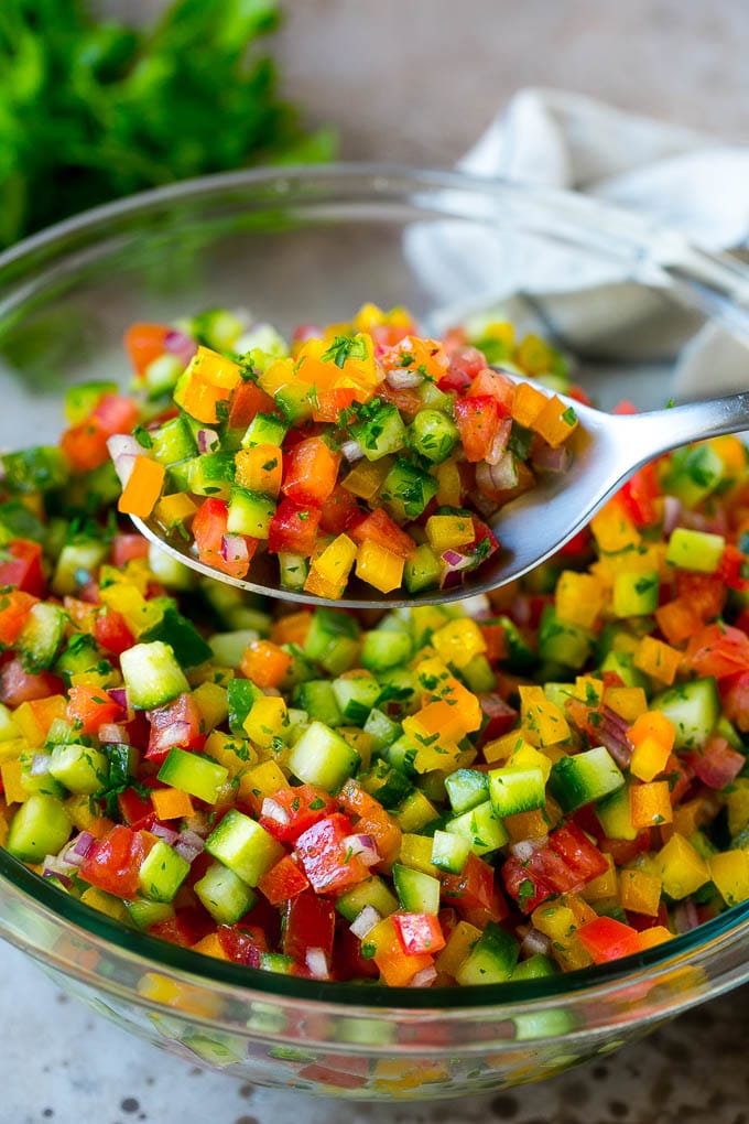 Israeli Salad Recipe | Cucumber Salad | Tomato Salad | Chopped Salad #salad #cleaneating #healthy #glutenfree #lowcarb #keto #sidedish #lunch #sadud A spoon holding up a serving of Israeli salad.