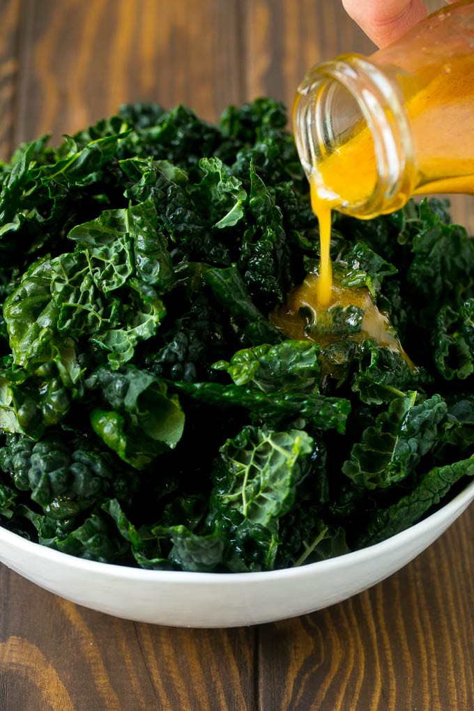 Apple Kale Salad Recipe | Kale Recipe | Fall Salad #kale #apples #bacon #salad #feta #dinner #lunch #sadud Dressing being poured over dinosaur kale leaves.