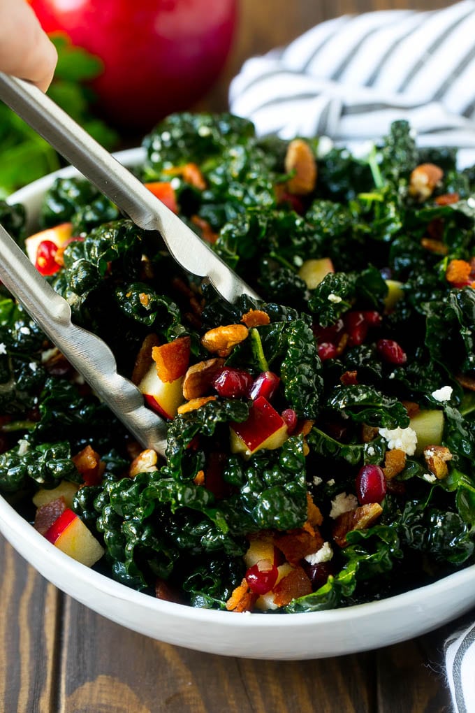 Apple Kale Salad Recipe | Kale Recipe | Fall Salad #kale #apples #bacon #salad #feta #dinner #lunch #sadud Tongs in a bowl of kale and apple salad.