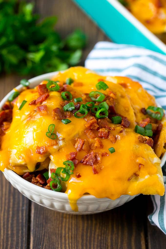 Pierogi Casserole Recipe | Potato Casserole #pierogis #casserole #bacon #cheddar #dinner #sadud A bowl of pierogi casserole topped with cheddar cheese and bacon.