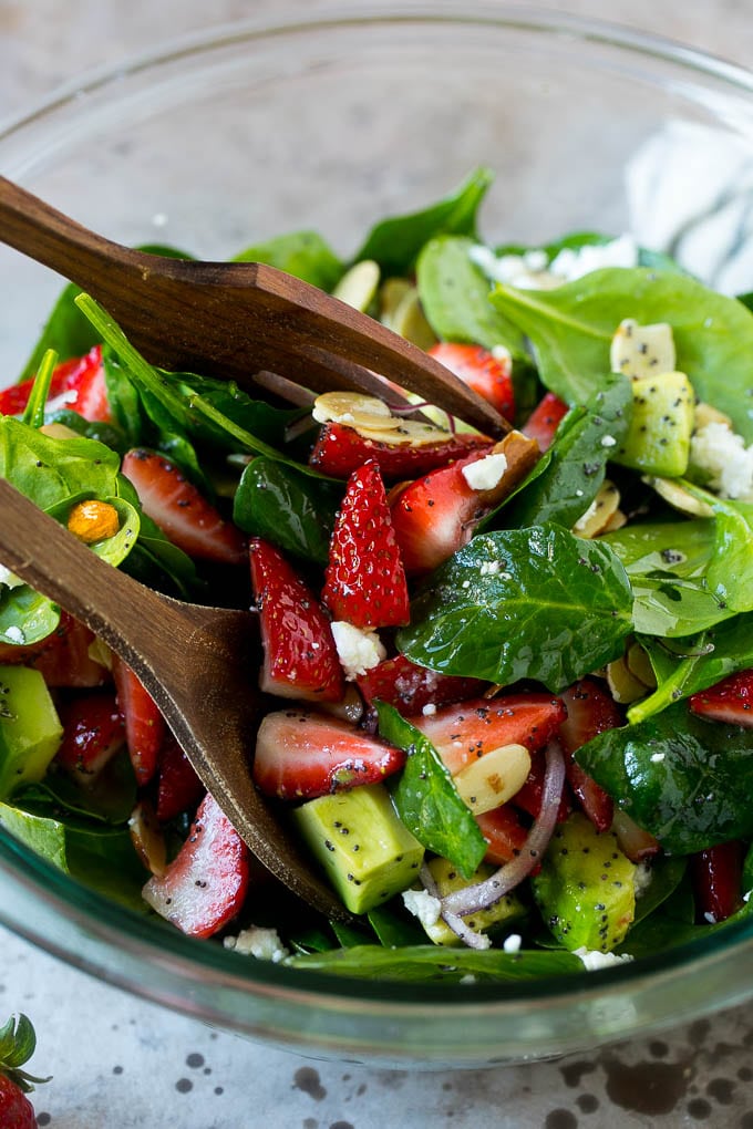 Strawberry Spinach Salad Recipe | Strawberry Salad | Spinach Salad #spinach #salad #strawberries #avocado #sadud Salad tongs in a bowl of spinach salad with strawberries.