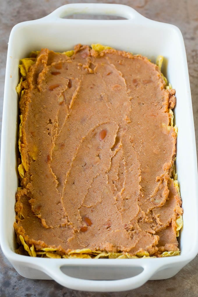 Taco Casserole Recipe | Mexican Casserole | Beef Casserole #casserole #tacos #beef #dinner #cheese #sadud A layer of refried beans on top of a crushed tortilla chips.