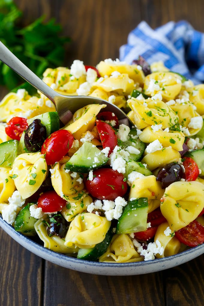 Greek Tortellini Salad Recipe | Pasta Salad | Tortellini Salad | Greek Salad #greek #tortellini #pasta #salad #cucumbers #olives #dinner #sadud A bowl of Greek tortellini salad with a serving spoon in it.
