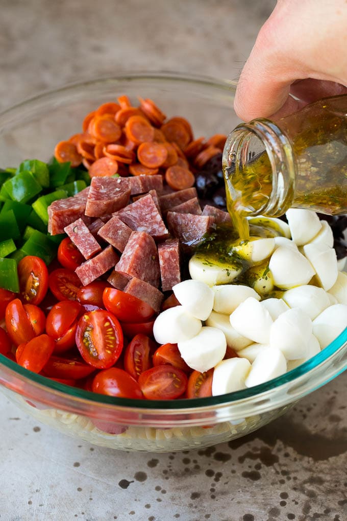 Italian Pasta Salad | Pasta Salad Recipe #pasta #salad #pastasalad #pepperoni #salami #olives #cheese #sidedish #sadud Italian dressing being poured over pasta salad ingredients.
