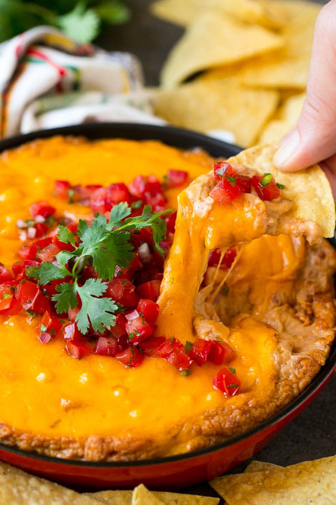 Bean Dip Recipe | Mexican Dip #dip #appetizer #mexicanfood #beans #cheese #sadud A tortilla chip scooping out a serving of Mexican bean dip.