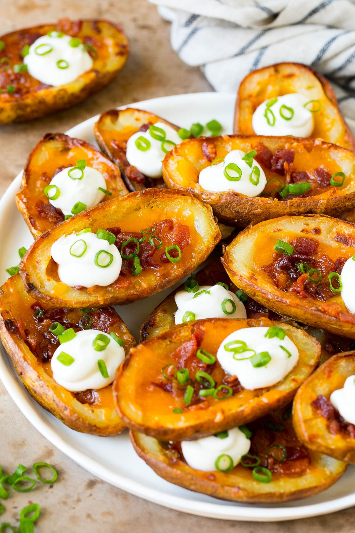 Potato Skins Recipe | Loaded Potatoes #potatoes #appetizer #snack #cheese #bacon #sadud A serving plate of potato skins topped with bacon and sour cream.