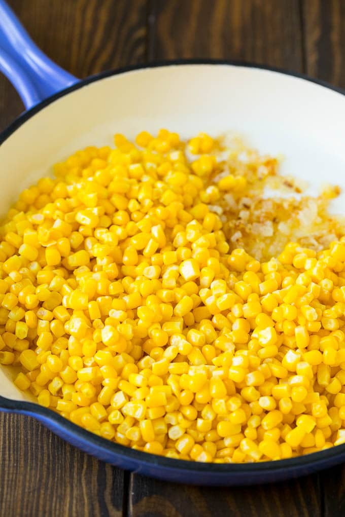 This creamed corn recipe consists of corn kernels simmered in cream sauce, then topped with crispy bacon and fresh herbs. Corn and sauteed onions in a pan.