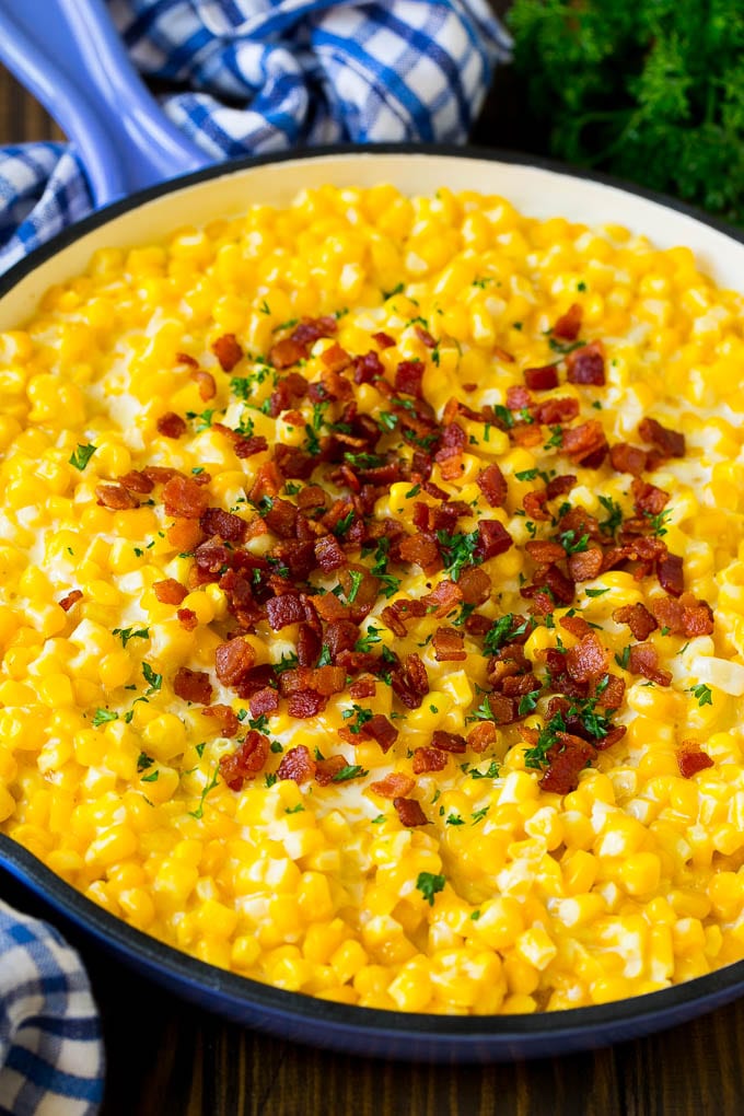 This creamed corn recipe consists of corn kernels simmered in cream sauce, then topped with crispy bacon and fresh herbs. Creamed corn in a pan with bacon and parsley.