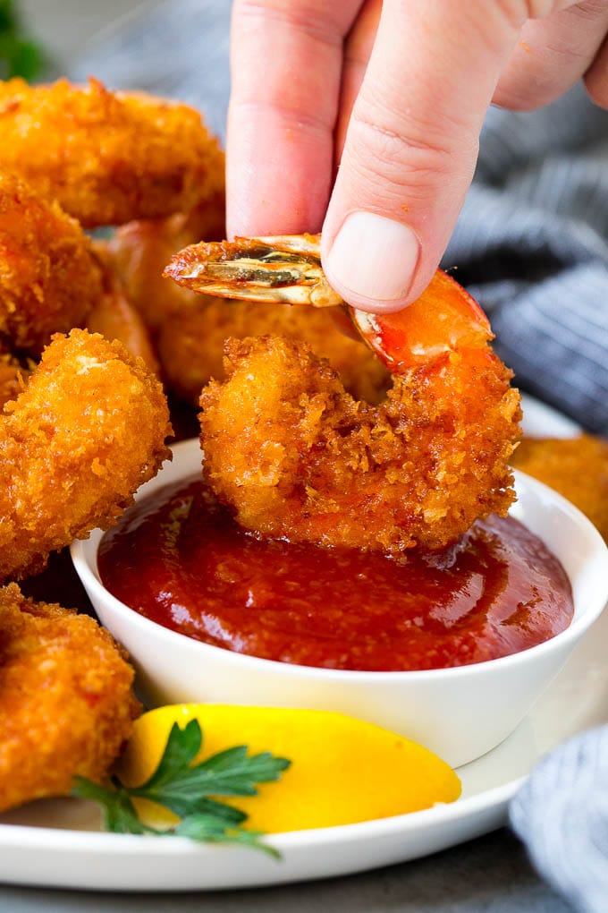 Fried Shrimp Recipe #shrimp #seafood #dinner #appetizer #sadud A hand dipping a shrimp into cocktail sauce.