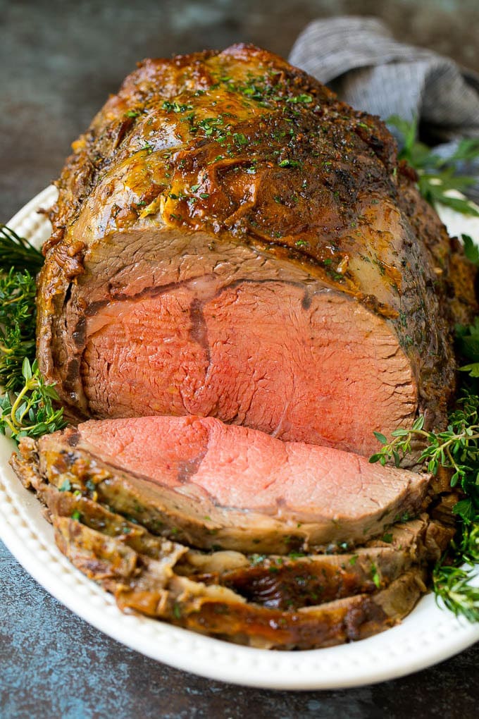 Prime Rib Recipe #primerib #beef #roast #dinner #thanksgiving #christmas #keto #lowcarb #sadud A sliced slow roasted prime rib roast surrounded by fresh herbs.