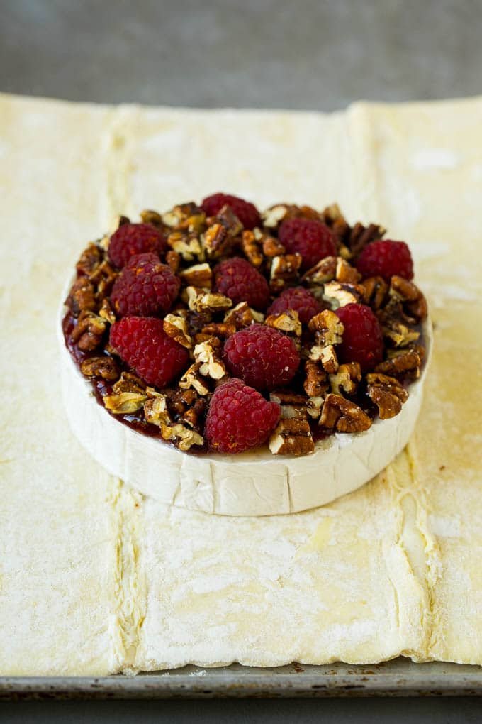 Baked Brie Recipe | Pastry Wrapped Brie #brie #cheese #appetizer #pecans #raspberries #sadud A wheel of cheese topped with jam, raspberries and pecans.