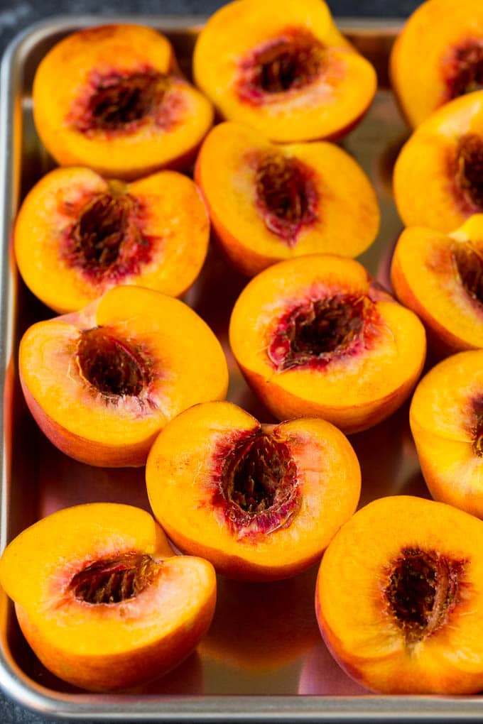 These grilled peaches are seared on the grill until tender and caramelized, then brushed with cinnamon honey for a sweet finish. Peaches cut in half on a sheet pan.