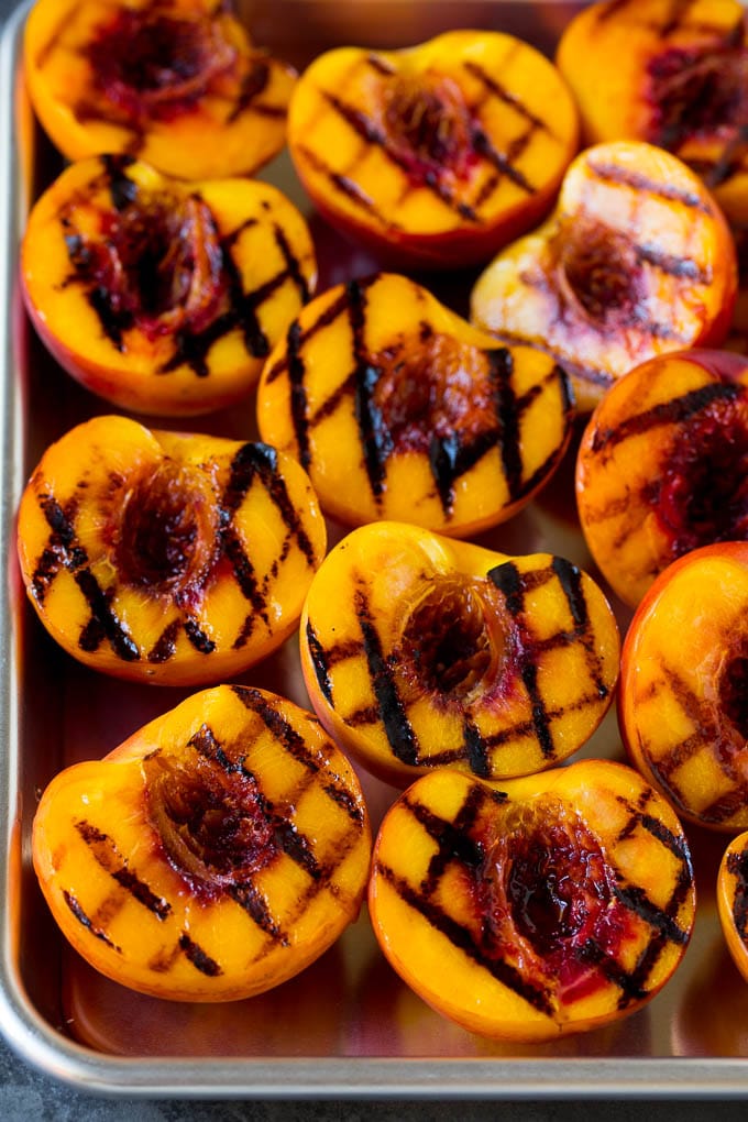 These grilled peaches are seared on the grill until tender and caramelized, then brushed with cinnamon honey for a sweet finish. Grilled peach halves arranged on a tray.