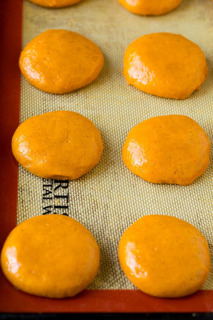 These soft pumpkin cookies bake up light and fluffy, and are topped with a decadent cream cheese frosting and colorful sprinkles. Rounds of cookie dough on a sheet pan.
