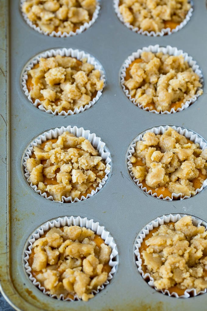 These pumpkin muffins are light and tender treats filled with plenty of pumpkin puree and spice, then topped with brown sugar streusel and baked to perfection. Pumpkin batter in a baking tin, topped with streusel.