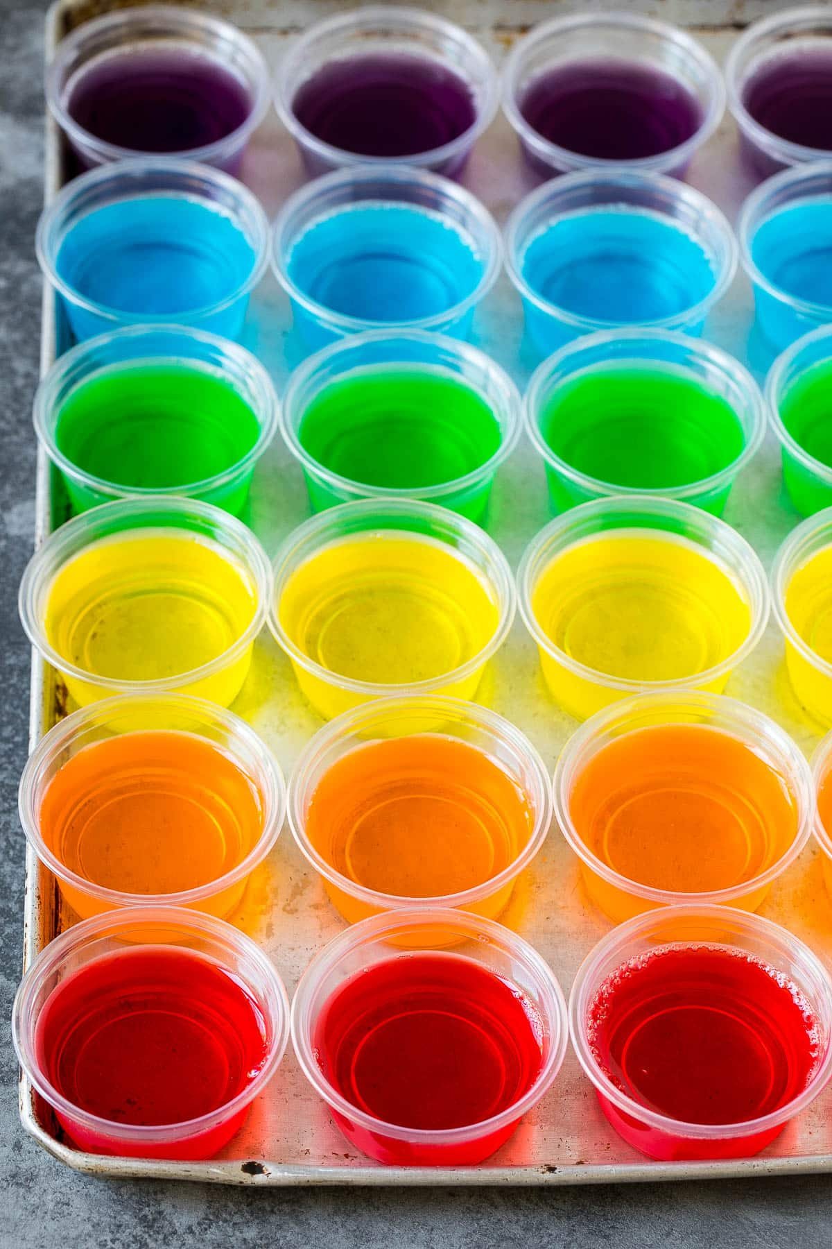 Rows of rainbow colored Jello shots lined up on a sheet pan.