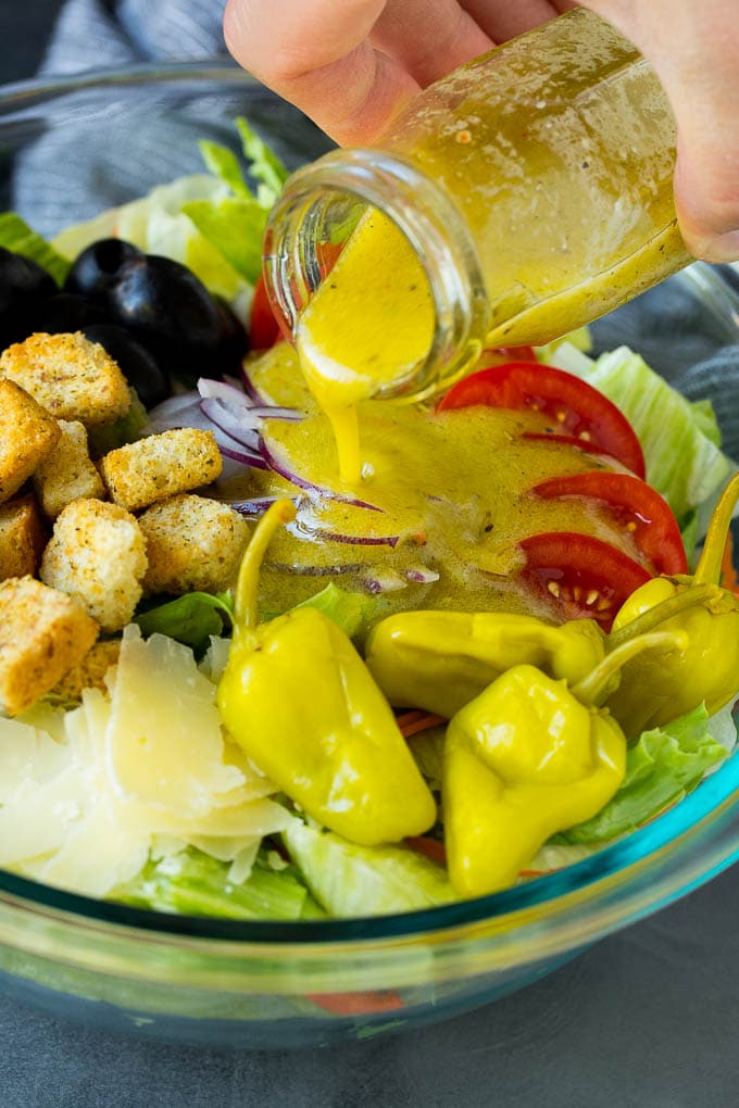 Olive Garden Salad Recipe | Italian Salad #salad #lettuce #olives #sidedish #dinner #sadud Dressing being poured over a bowl of salad.