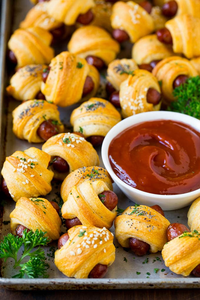 Pigs in a Blanket Recipe #hotdogs #appetizer #snack #comfortfood #sadud A sheet pan of pigs in a blanket, garnished with parsley and served with ketchup.