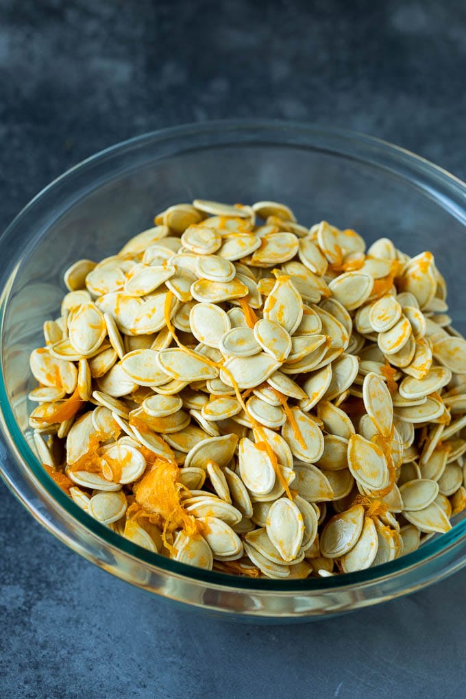 These roasted pumpkin seeds are coated in butter and seasonings, then baked until golden brown. Pumpkin seeds and pumpkin flesh in a bowl.