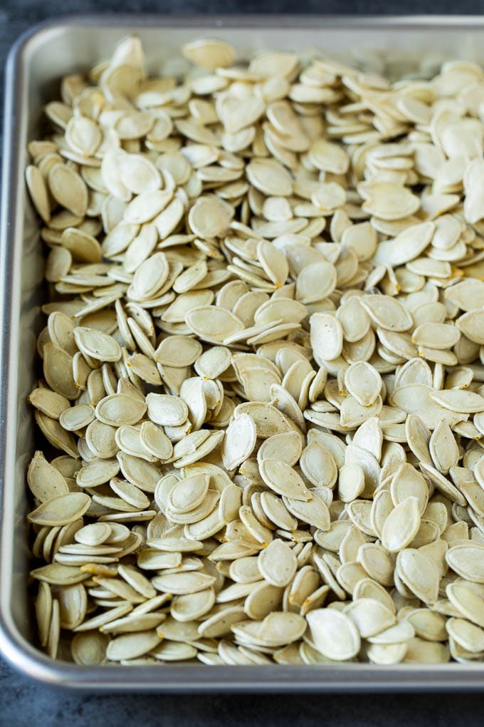 These roasted pumpkin seeds are coated in butter and seasonings, then baked until golden brown. Seeds coated in seasonings and spread on a sheet pan.