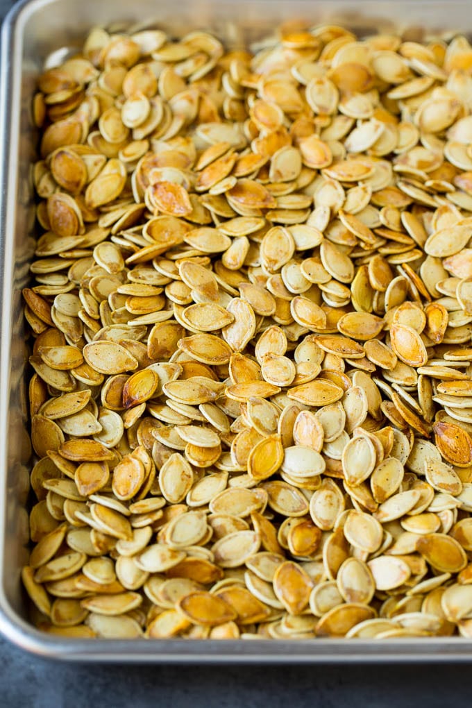 These roasted pumpkin seeds are coated in butter and seasonings, then baked until golden brown. Roasted pumpkin seeds on a sheet pan.