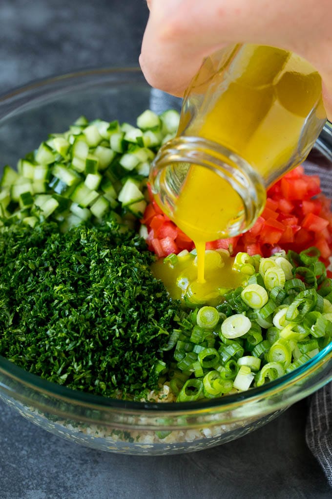 Tabbouleh Salad | Tabouli #salad #wheat #tomatoes #cucumber #healthy #sidedish #dinner #sadud Dressing being poured into a bowl of bulgur wheat salad.