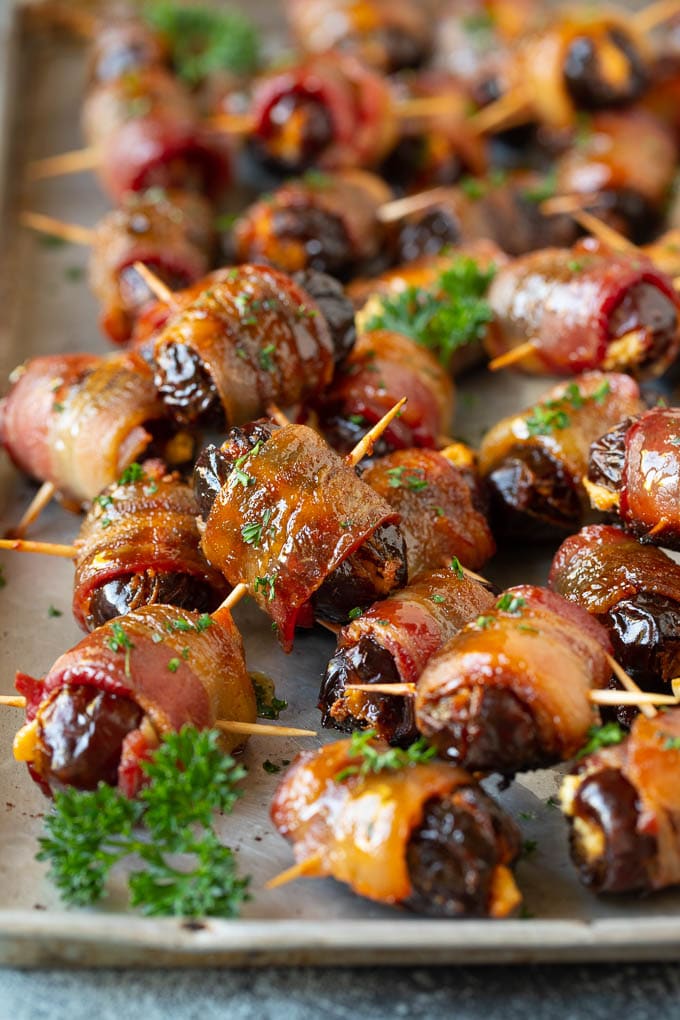 Bacon Wrapped Dates #appetizer #bacon #dates #cheese #sadud Bacon wrapped dates on a sheet pan garnished with parsley.