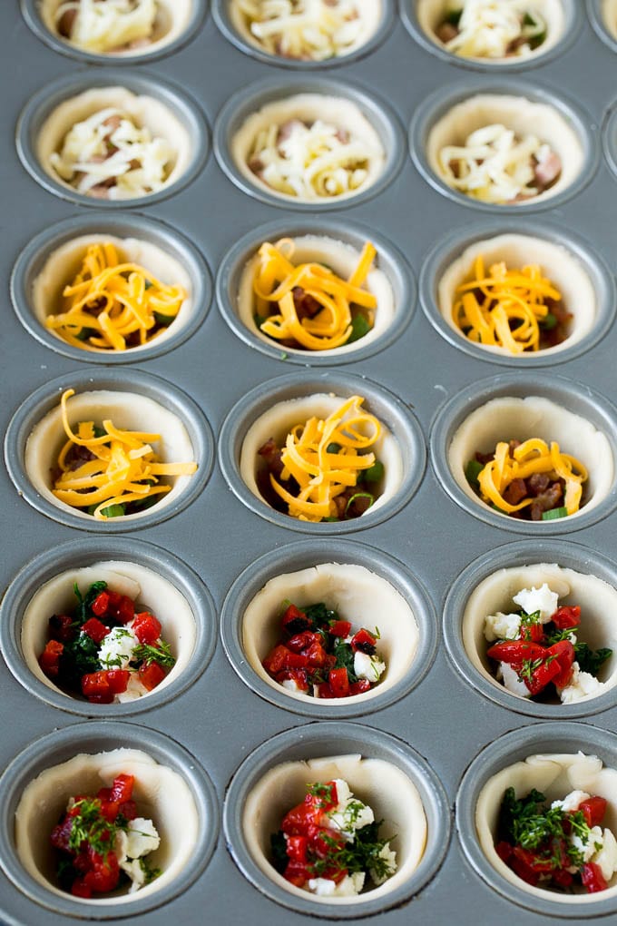 Mini Quiche Recipe #eggs #breakfast #brunch #appetizer #sadud Muffin tins filled with pie crust, vegetables, meat and shredded cheese.