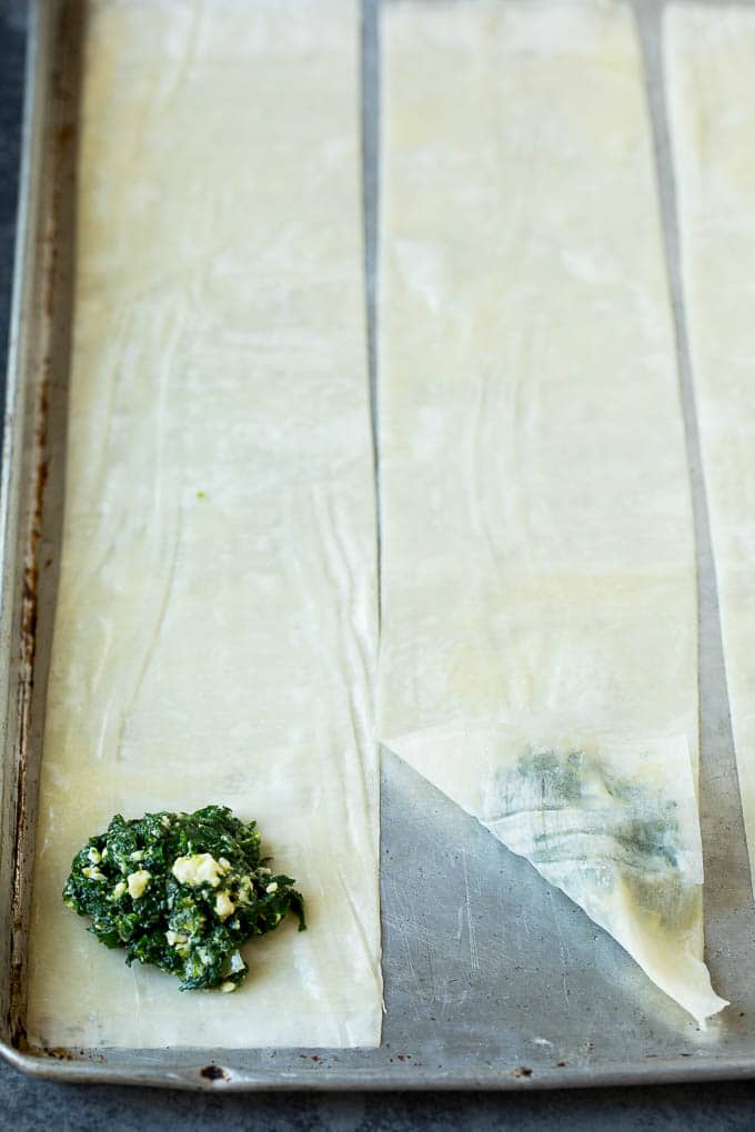 Spanakopita Recipe #appetizer #snack #spinach #cheese #sadud Strips of phyllo dough with spoonfuls of filling on top.