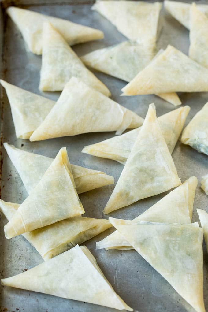 Spanakopita Recipe #appetizer #snack #spinach #cheese #sadud Folded stuffed phyllo triangles on a sheet pan.