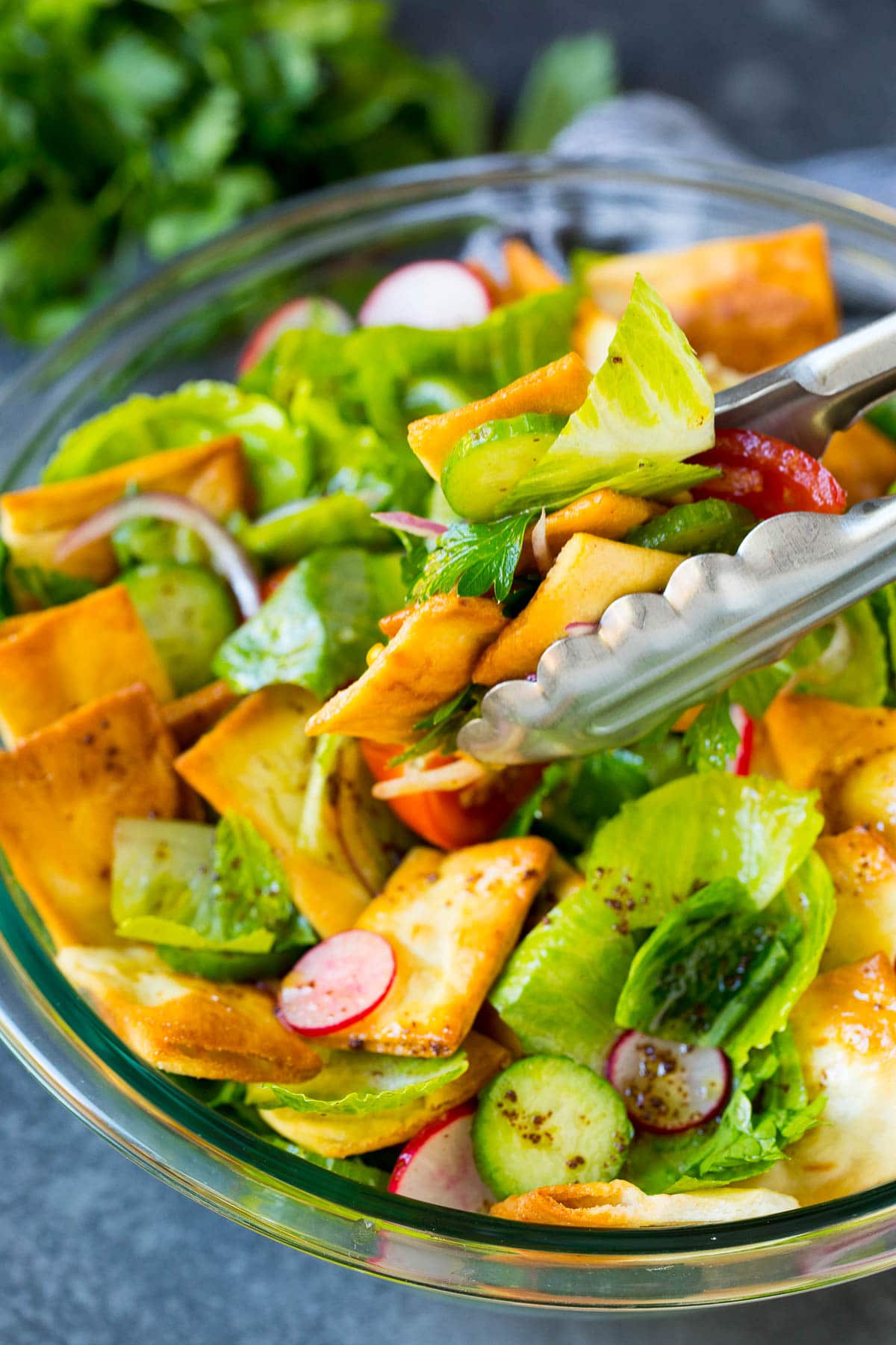 Tongs serving a portion of fattoush salad.