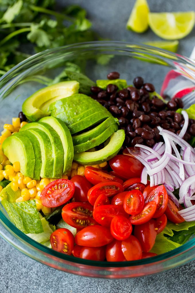 Mexican Salad Recipe #salad #corn #beans #avocado #tomatoes #sadud Lettuce, tomatoes, onion, corn, avocado and black beans in a bowl.