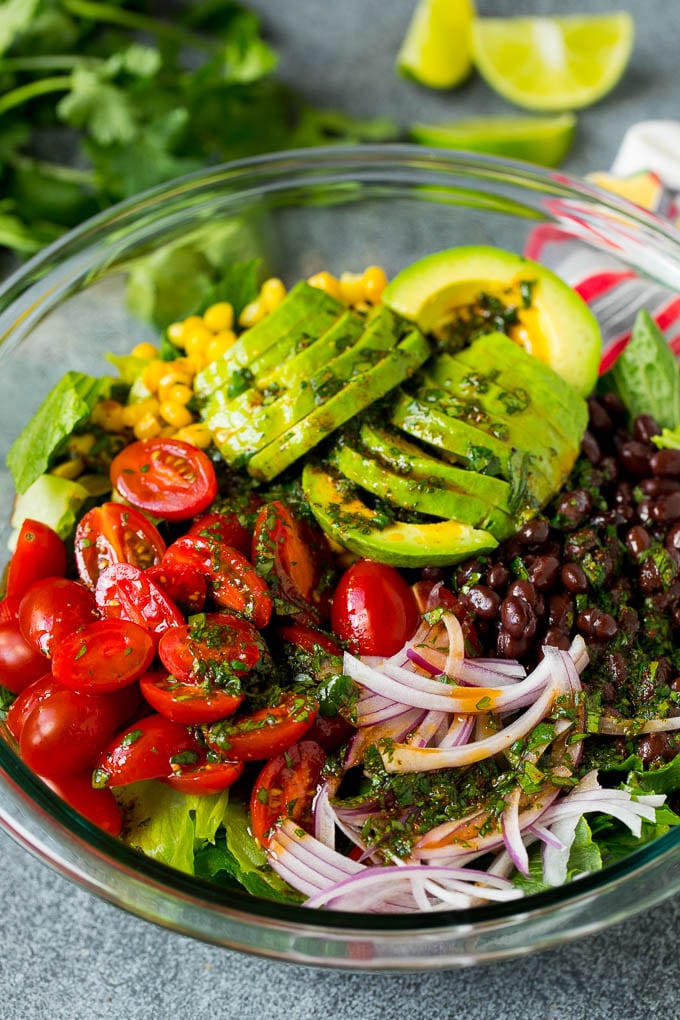 Mexican Salad Recipe #salad #corn #beans #avocado #tomatoes #sadud Dressing poured over a bowl of lettuce, tomatoes, avocado and beans.