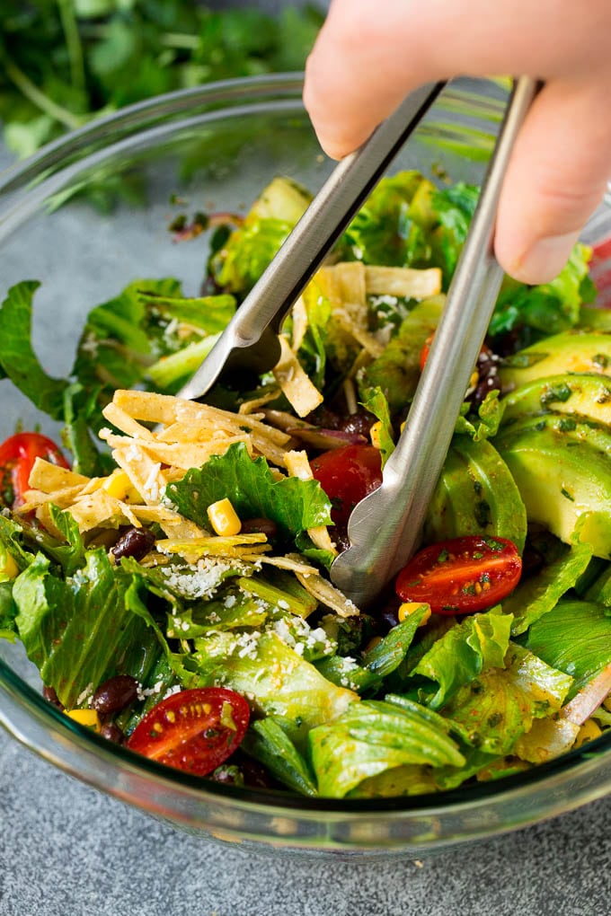 Mexican Salad Recipe #salad #corn #beans #avocado #tomatoes #sadud Tongs serving up a portion of Mexican salad.