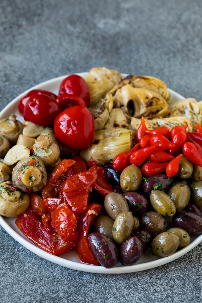 This mezze platter is filled with Mediterranean delicacies including dolmas, hummus, vegetables, pita bread and salads. #appetizer #sadud A plate of olives, peppers and grilled artichokes.