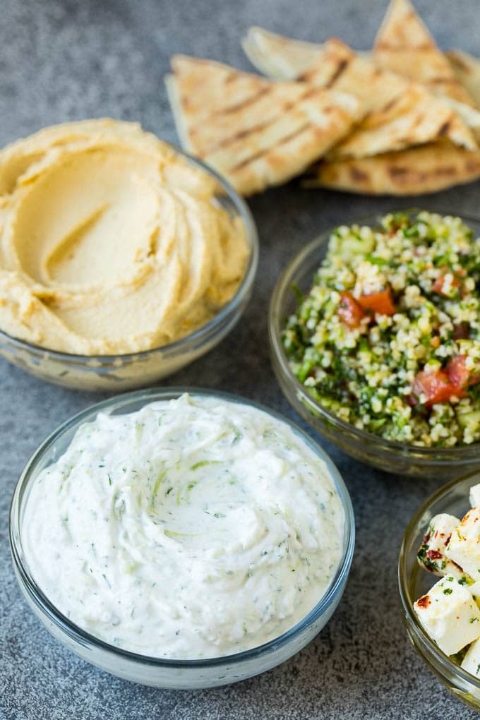 This mezze platter is filled with Mediterranean delicacies including dolmas, hummus, vegetables, pita bread and salads. #appetizer #sadud Bowls of hummus, tzatziki and tabbouleh.