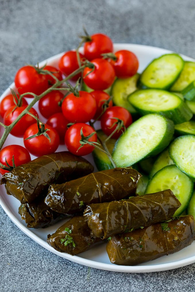 This mezze platter is filled with Mediterranean delicacies including dolmas, hummus, vegetables, pita bread and salads. #appetizer #sadud A plate of cherry tomatoes, cucumber slices and dolmas.
