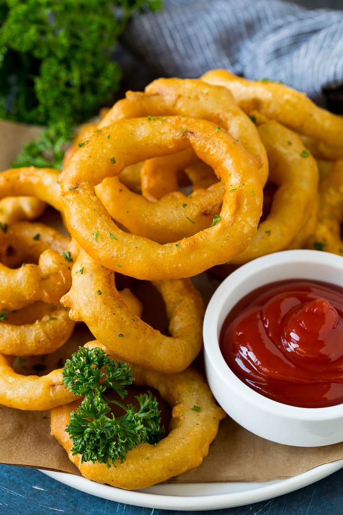 Crispy homemade onion rings that are fried in a flavorful beer batter. #onions #sadud #appetizer Fried onion rings on a plate with a side of ketchup.