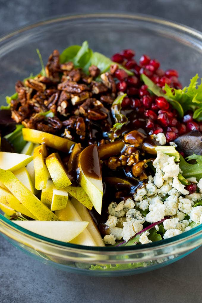 Pear Salad Recipe #salad #pears #fall #winter #dinner #sadud Balsamic dressing poured over a bowl of mixed greens, fruit and pomegranate seeds.